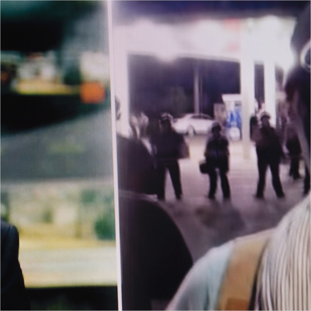 Detail thumbnail of photograph of a screen showing split feeds: one is in a newscaster studio, one is a reporter on-site with armed forces behind her. 
